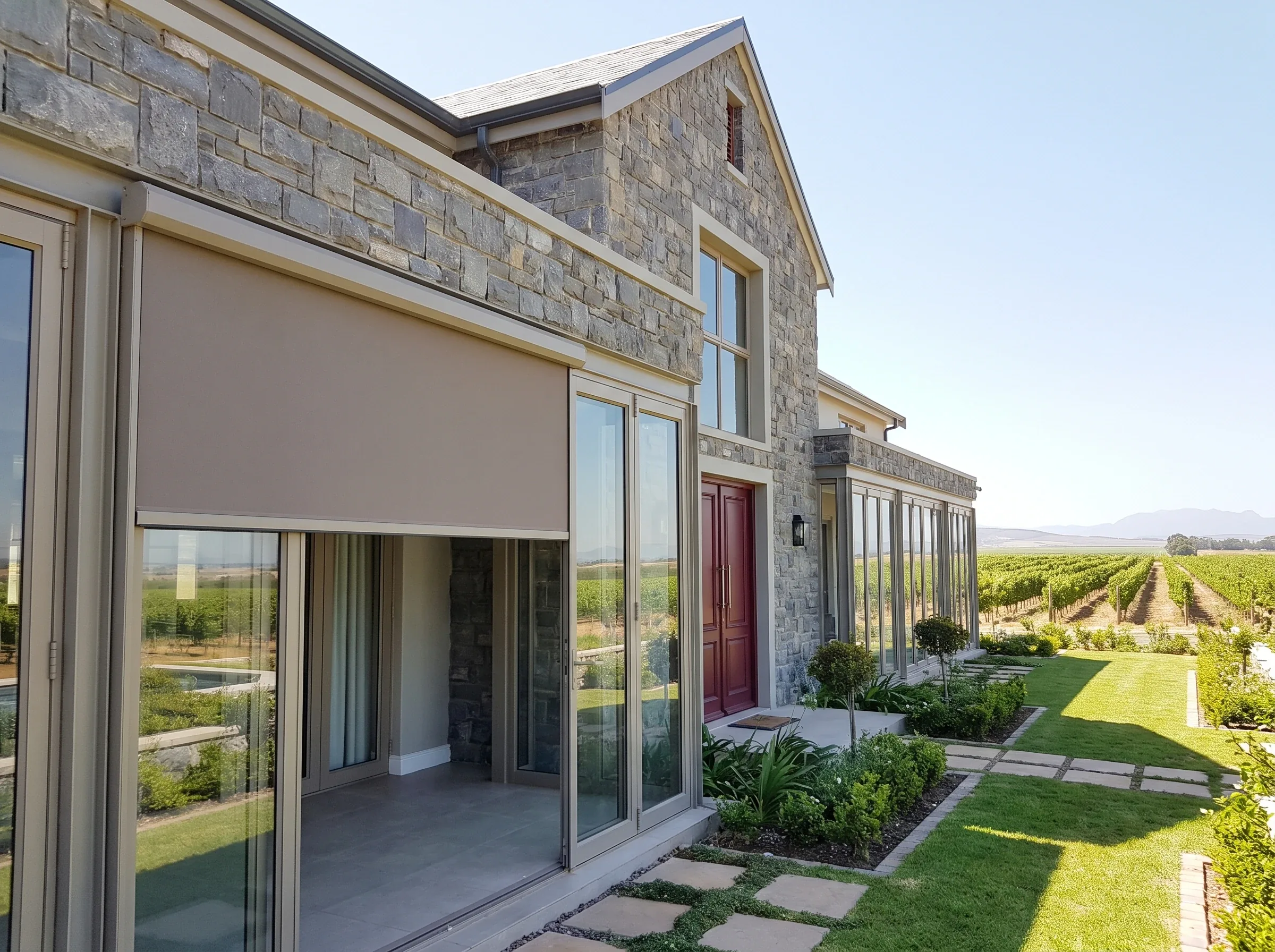 Stone-clad Durbanville home with a retractable awning over a covered patio, vineyards visible beyond the garden