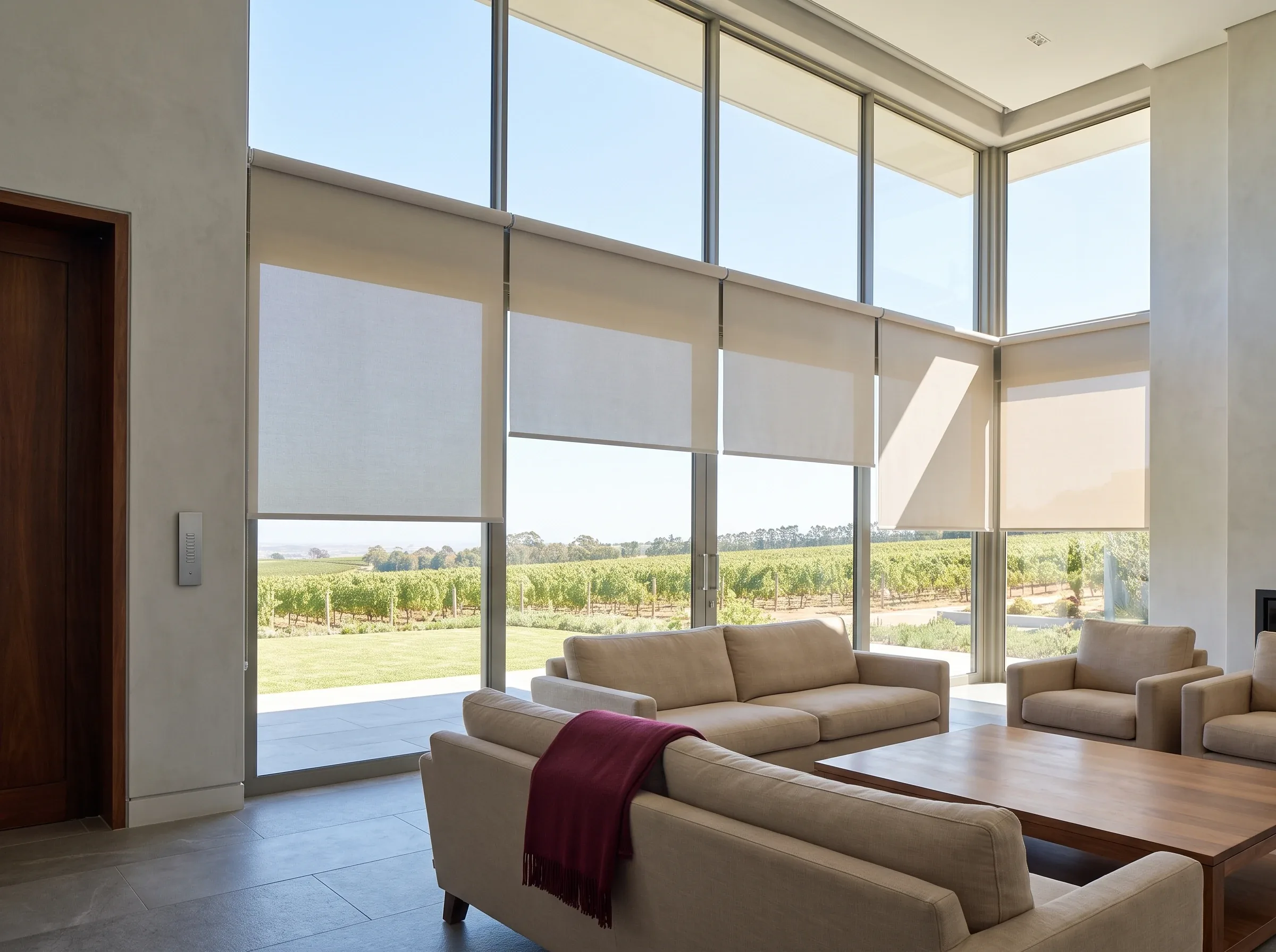 Row of tall motorised roller blinds lowered in a double-volume glass living room